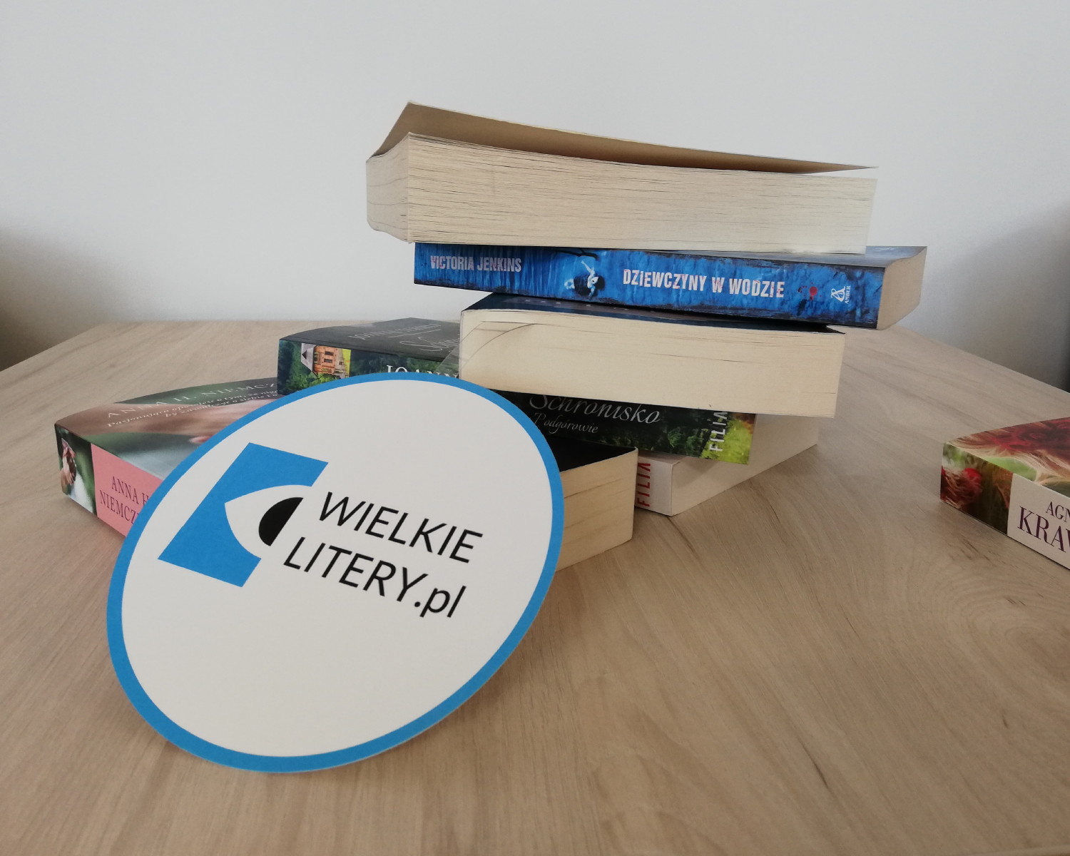 Kilka książek na stoliku, z przodu okrągłe logo Wielkie Litery.pl