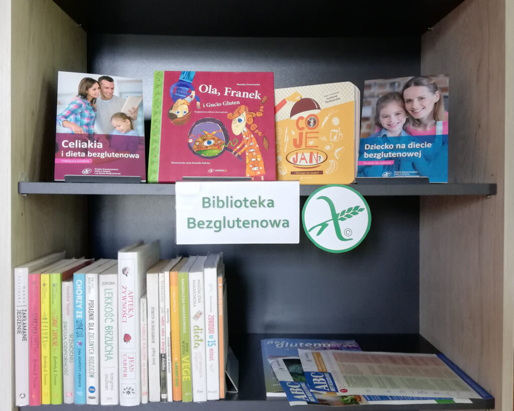 Półka z książkami, podpisana Biblioteka Bezglutenowa, wyeksponowane tytuły o celiakii i diecie bezglutenowej